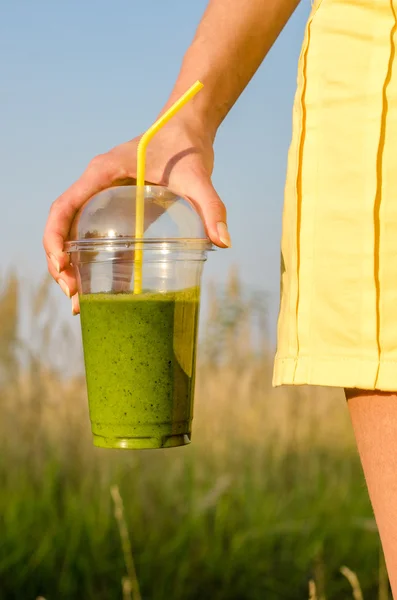 Energía verde y batido nutricional en la mano sobre fondo borroso naturaleza y cielo azul — Foto de Stock