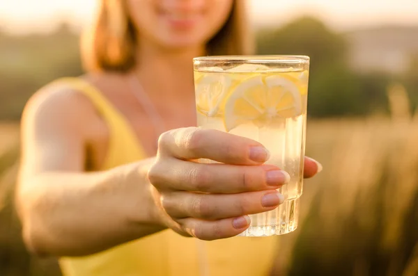 Limonada amarela nutricional na mão de uma jovem em uma camisa de esportes amarelos no fundo borrado natureza — Fotografia de Stock