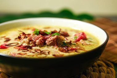 Soto Betawi, kremalı biftek ya da hindistan cevizi sütü, baharat, domates, soğan, arpacık soğanı ve Endonezya spesiyalitesinden yapılmış sakatat çorbası. Altta muz yaprağı ve bardak altlığı var. yakınlaştırılmış görünümü kapat