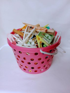 Elbise askılarıyla dolu pembe delikli bir sepet. Çamaşırları yıkadıktan sonra kurutmak için beyaz arka planda yeşil bir sepete iğneler..