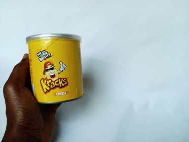 Kumasi, Gana - 9 Aralık 2025: Beyaz arka planda şeffaf kapaklı silindirik kağıtta Krakks patates cipsi tutan Afrikalı insan eli. Kracks logotype ve peynir aromalı sarı kısa tüp manzarası. Malezya, Gıda İmparatorluğu 'nun ürünü. Birlikte