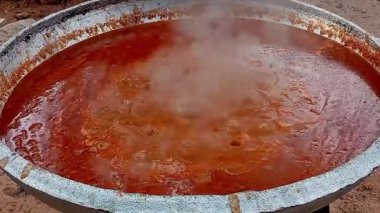 Kırmızı domates yahnisini büyük metal bir tencerede hazırlıyorum. Sıcak yağda pişirirken çıkan buharlı domates yahnisi. Gıda süreci.