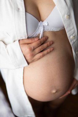 Hamile bir kadın, elleri sırtında karnını tutan hamile bir kadın. Beyaz arka plan. Genç hamile bir kadın karnına dokunuyor, güzel bir hamile göbeğine yaklaşıyor..