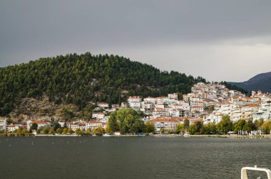 Kastoria, Yunanistan. Bulutlu bir sonbahar gününde, Kastoria şehrinin göl kenarındaki panoramik manzarası, sakin sularda ve tepedeki geleneksel evlerde yansımalar..
