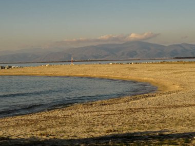 Sahil manzarası. Sahil manzarası. Sabahın erken saatlerinde açık mavi bir gökyüzü altında kumlu bir sahil, sakin bir deniz ve sisli dağların yer aldığı sakin bir kıyı manzarası..