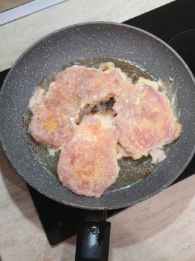 Top-down view of pork cutlets frying in oil on a non-stick pan