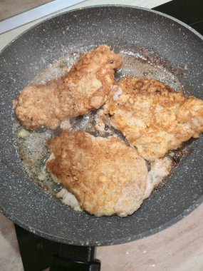 Top-down view of pork cutlets frying in oil on a non-stick pan