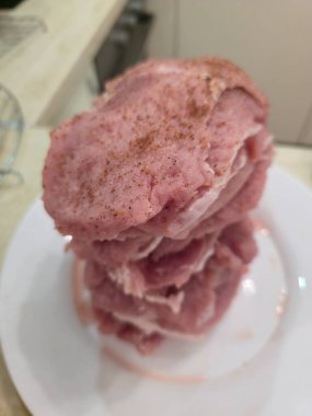 Tall stack of raw seasoned thin pork cutlets on white plate