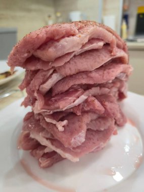 Tall stack of raw seasoned thin pork cutlets on white plate