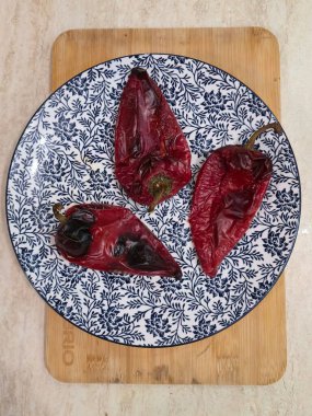 Top-down view of three roasted red peppers on patterned blue and white plate