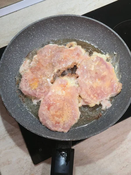 Top-down view of pork cutlets frying in oil on a non-stick pan