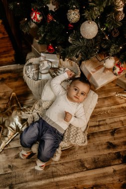 Güzel dekore edilmiş bir Noel ağacının yanında, örülmüş battaniyenin üzerinde uzanmış sevimli bir çocuk ve yukarıdan güzel ve şenlikli bir tatil portresi yakalıyor. Yeni yıl, Noel