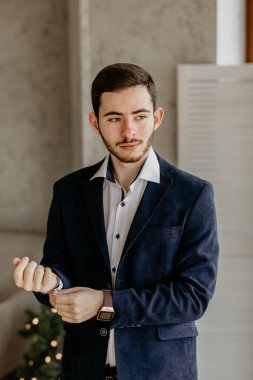 Şık mavi ceketli ve beyaz gömlekli yakışıklı bir gencin portresi akıllı saatini ayarlıyor, bir Noel partisine ya da tatil etkinliğine hazırlanıyor.