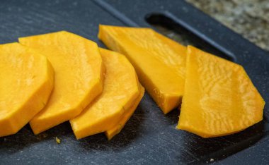 Çiğ, soyulmuş ve ince dilimlenmiş parlak turuncu tereyağlı kabak ya da balkabağı parçaları siyah bir kesme tahtasına dizilmiş, kızartılmaya ya da sonbahar yemekleri pişirmeye hazır.