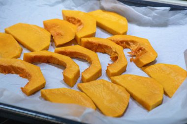 Çiğ, canlı portakal kabağı dilimleri ve parşömen kağıdıyla kaplanmış kaşık dilimleri, kızarma, pişirme veya sonbahar tatlısı pişirme için hazırlanmış.