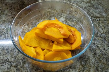 Kalın, çiğ, canlı portakallı balkabağı dilimleri ya da takozlarla dolu cam bir kasenin tepesinde püre yapmak ya da sonbahar tatlısını pişirmek için hazırlanmış.