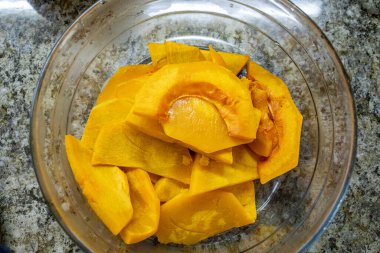 Kalın, çiğ, canlı portakallı balkabağı dilimleri ya da takozlarla dolu cam bir kasenin tepesinde püre yapmak ya da sonbahar tatlısını pişirmek için hazırlanmış.