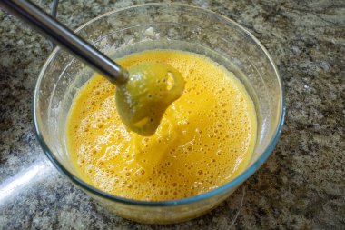 Parlak turuncu balkabağı püresi ya da hamuru cam bir kaseye karıştırarak baloncuklar ve fırın için yumuşak bir karışım oluşturan bir mikserin yakın çekimi