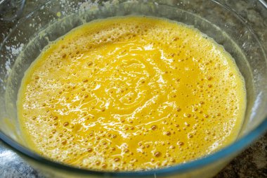 Parlak sarı ve turuncu, pürüzsüz balkabağı ya da yumurta hamuru içeren ve kek, tatlı ya da güveç pişirmeye hazır olan büyük bir cam kasenin hemen üstünde.