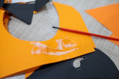 Kesilen turuncu kağıda siyah şekilli beyaz yapıştırıcı ve kağıt işçiliğini sembolize eden kırmızı yapıştırıcı.