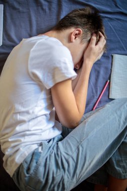 Yüzü ellerine gömülmüş, okul veya ev ödevleri yüzünden hayal kırıklığına uğramış, stresli bir genci yatakta yatarken gördüm.