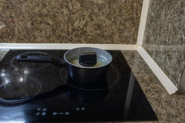 Modern elektrikli seramik hob kapağı olan siyah tencere, granit mutfak tezgahında yemek pişiriyor.