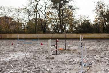 Çamurlu ve boş binicilik gösterisi renkli engellerle atlama arenası ve bulutlu bir sonbahar gününde sarı bir çit.