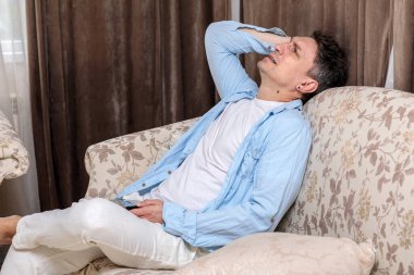 Yorgun ya da stresli orta yaşlı bir adam desenli bir kanepede dinleniyor, kafasını kaldırıyor ve elini alnına koyup derin derin düşünüyor.