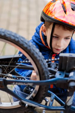 Güvenli bir kaskla bisikletin tekerleğini ve zincirini tamir eden ya da inceleyen, dışarıda mekanik öğrenen bir çocuk.