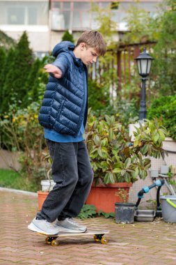 Genç bir çocuk dışarıda kaykayla bir numara yapıyor ya da zıplıyor, dinamik hareketler ve hareketler sergiliyor.