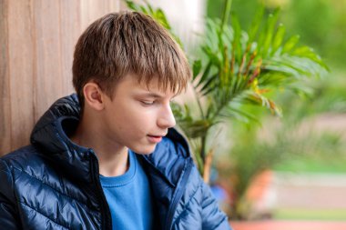 Mavi ceketli düşünceli bir gencin, gölgeli bir verandaya dikkatlice bakan portresi.