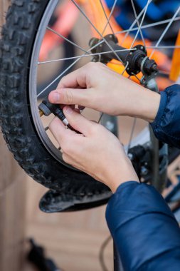 Patlak bir bisiklet lastiğini şişirmek için kırmızı el pompası kullanan bir çocuğun ellerine yakın çekim.