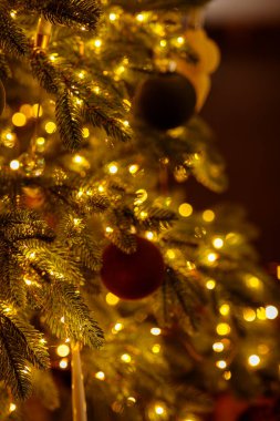 Sıcak altın peri ışıkları ve kadife kırmızısı ve yeşil süslemelerle süslenmiş bir Noel ağacının yakın çekimi zengin bir bokeh yaratıyor.