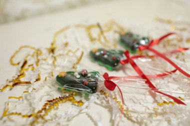 Üç noel ağacı şekilli lolipoplar ya da kırmızı kurdelelerle bağlanmış şekerlemeler, beyaz ve altın renginde konfetiler üzerinde duruyor.