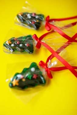 Kırmızı kurdeleli üç noel ağacı şekilli lolipoplar. Fotokopi alanı ve üst görünümü olan canlı sarı bir zemin üzerinde yatıyorlar.