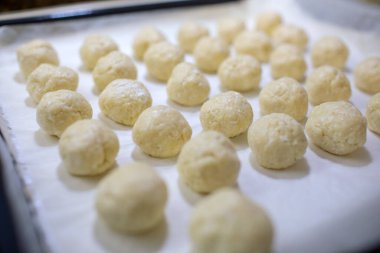 Geleneksel Bulgar solenkisi için pek çok küçük ham hamur topunun genel çekimi - tuzlu peynirli hamur tatlısı, parşömen kağıdıyla fırın için hazır bir fırın kağıdının üzerine dizilmişti.