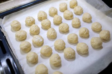 Geleneksel Bulgar solenkisi için pek çok küçük ham hamur topunun genel çekimi - tuzlu peynirli hamur tatlısı, parşömen kağıdıyla fırın için hazır bir fırın kağıdının üzerine dizilmişti.