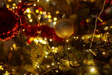 Işıldayan beyaz ışıklar ve zengin kırmızı süslemelerle çevrili bir Noel ağacından sarkan pırıl pırıl pırıl pırıl pırıl bir altın parıltı.