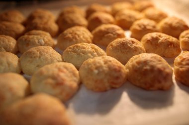 Yukardan gelen sıcak ve yoğun ışıkla aydınlatılan, parşömen kağıdının üzerinde duran altın, yeni pişmiş peynirli pufların yakın çekimi.