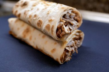 Koyu mavi bir tabağa istiflenmiş iki sıcak, yeni hazırlanmış shawarma ya da tat yakın plan, kızarmış lavaşın içindeki ızgara et ve lezzetli sosu gösteriyor.