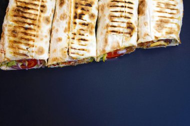 Dolguyu ortaya çıkarmak için dizilmiş ve dilimlenmiş dört taze ızgara shawarma ya da şiş ambalaj kağıdının yatay yukarıdan aşağı görüntüsü, fotokopi alanı olan koyu, minimalist bir mat yüzeyine kurulmuş.