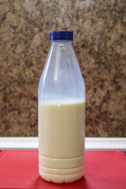 Mutfakta kırmızı bir kesme tahtasının üzerinde duran taze beyaz süt ya da süt ürünü içeren plastik şişe, basit bir ev bakkalı ve içeride kahvaltı için sağlıklı kalsiyum besin.