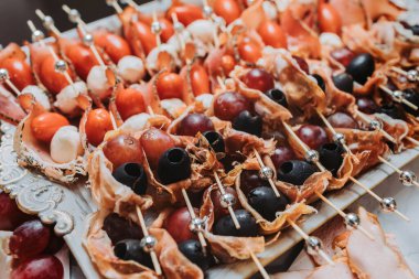 Prosciutto jambonu, kırmızı üzüm, mozzarella topları ve gümüş şişler üzerinde siyah zeytinler, düğün için profesyonel yemek servisi ya da kapalı alanda yapılan kutlama ile aperatifleri kapatın.