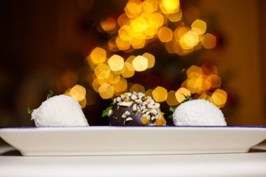 Şenlikli bir Noel ağacı arka planında çikolata kaplı çilek ve hindistan cevizi taneleri. Zarif bir bayram tatlısı, tatlı hediye konsepti.