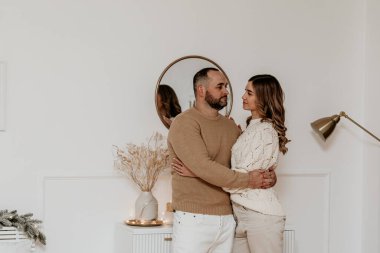 Örgü kazaklı romantik genç bir çift şık beyaz bir yatak odasında birbirlerine sarılıp bakıyorlar. Birlikte kış tatillerini, evde aşk ve ilişki kavramlarını kutluyorlar.