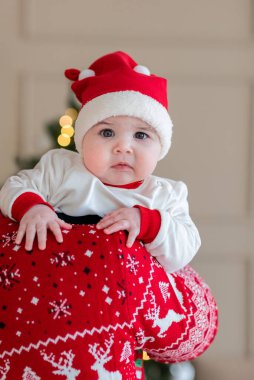Noel Baba şapkası takmış, Noel şenlikli bir kazakla birinin omzuna yaslanmış şirin bir bebeğin portresi. Kış tatilini evde kutlayan sevimli bir bebek.