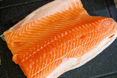 Taze çiğ somon filetosunu siyah bir kesim tahtasının üzerinde kapayın. Mutfakta pişirmek için hazırlanan organik turuncu balık eti ve pullarını gösterin.