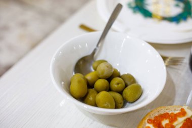 Beyaz ekmeğin üstünde kırmızı havyarlı sandviçler ve bayram kutlaması ya da aile yemeği için beyaz bir masada servis edilen bir kase yeşil zeytin.