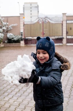 Mutlu çocuk kışın dışarıda kar atıyor, neşeli çocuk rahat bir konutun bahçesinde ilk kar yağışının keyfini çıkarıyor, kar taneleriyle neşeli bir çocukluk anı, soğuk mevsimlik yaşam tarzı