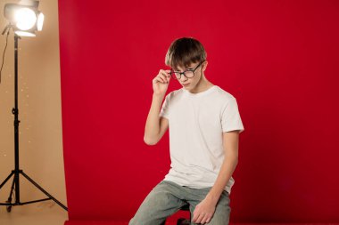 Stüdyoda parlak kırmızı arka planda poz veren beyaz tişörtlü gülümseyen genç çocuk, kendine güvenen, doğal duyguları olan sıradan bir gençlik portresi ve kopyalama alanı.